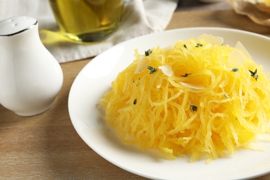 Plate with cooked spaghetti squash on wooden table, closeup