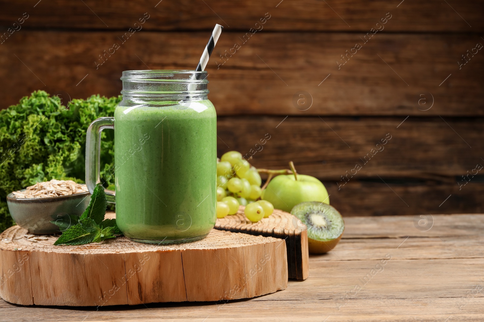 Photo of Mason jar of fresh green smoothie and ingredients on wooden table, space for text