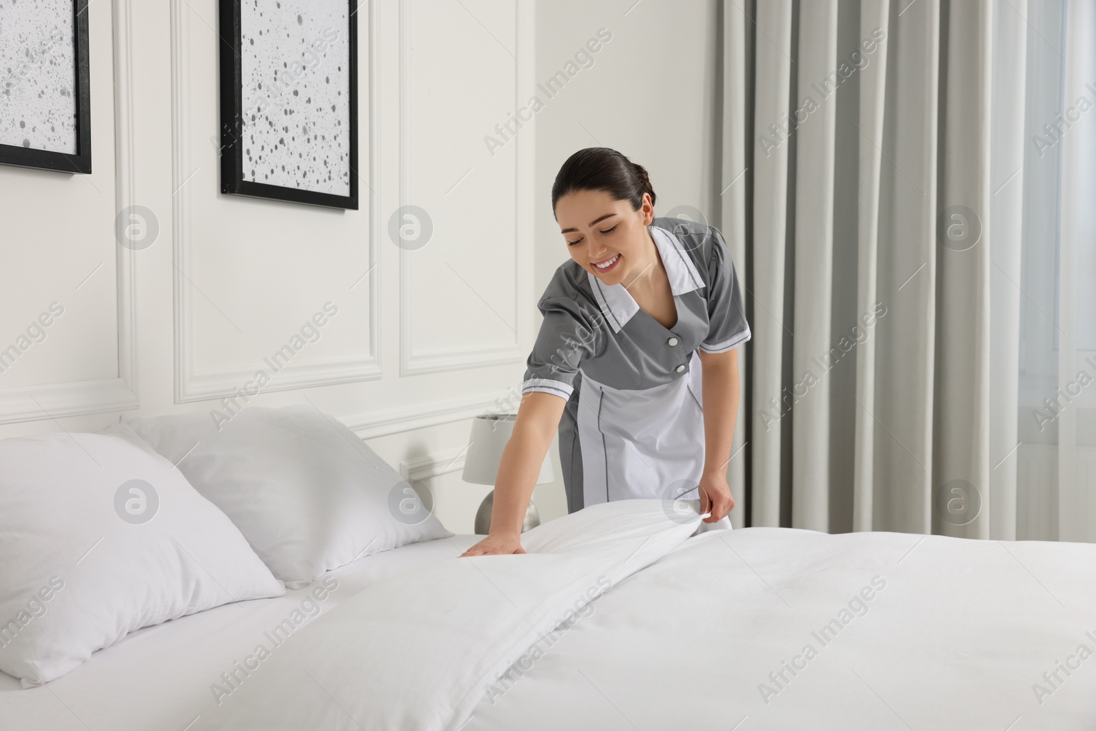 Photo of Young maid making bed in hotel room