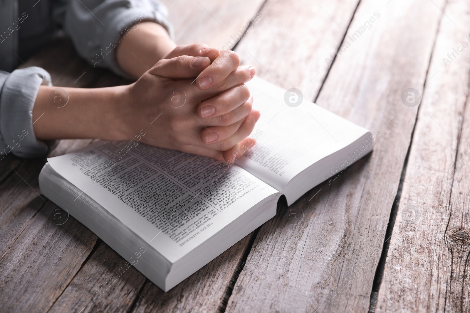 Photo of Religion. Christian woman praying over Bible at wooden table, closeup