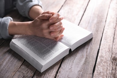 Religion. Christian woman praying over Bible at wooden table, closeup