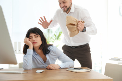 Photo of Man popping paper bag behind his sleeping colleague in office. April fool's day