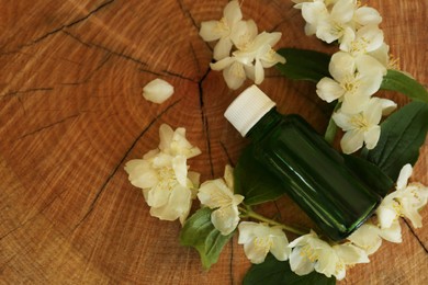 Photo of Bottle of jasmine essential oil and white flowers on wooden stump, above view. Space for text