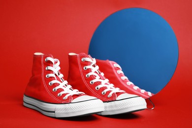 Pair of new stylish sneakers and mirror on red background
