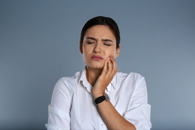 Woman suffering from toothache on grey background