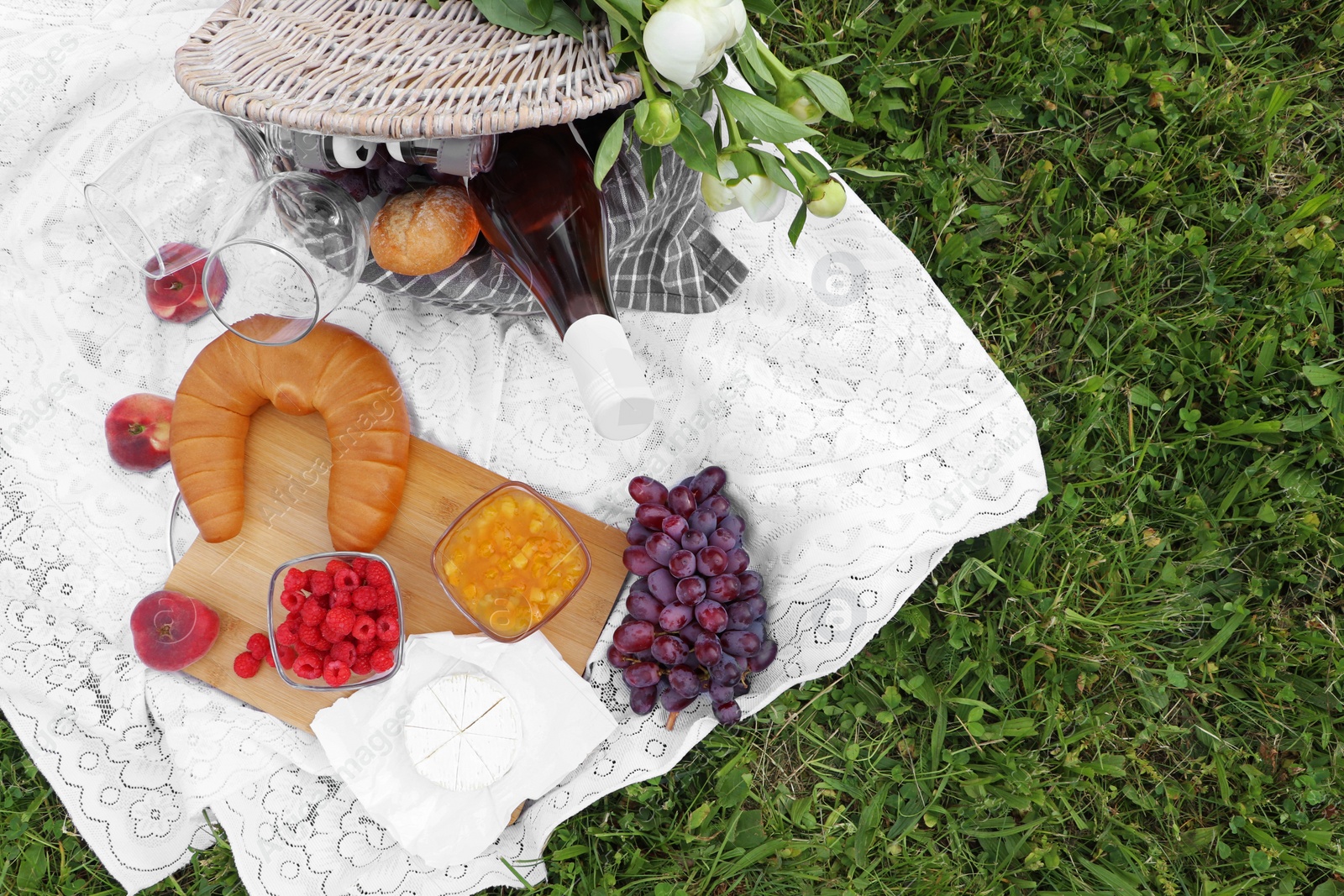 Photo of Picnic blanket with tasty food, flowers and cider on grass outdoors, flat lay