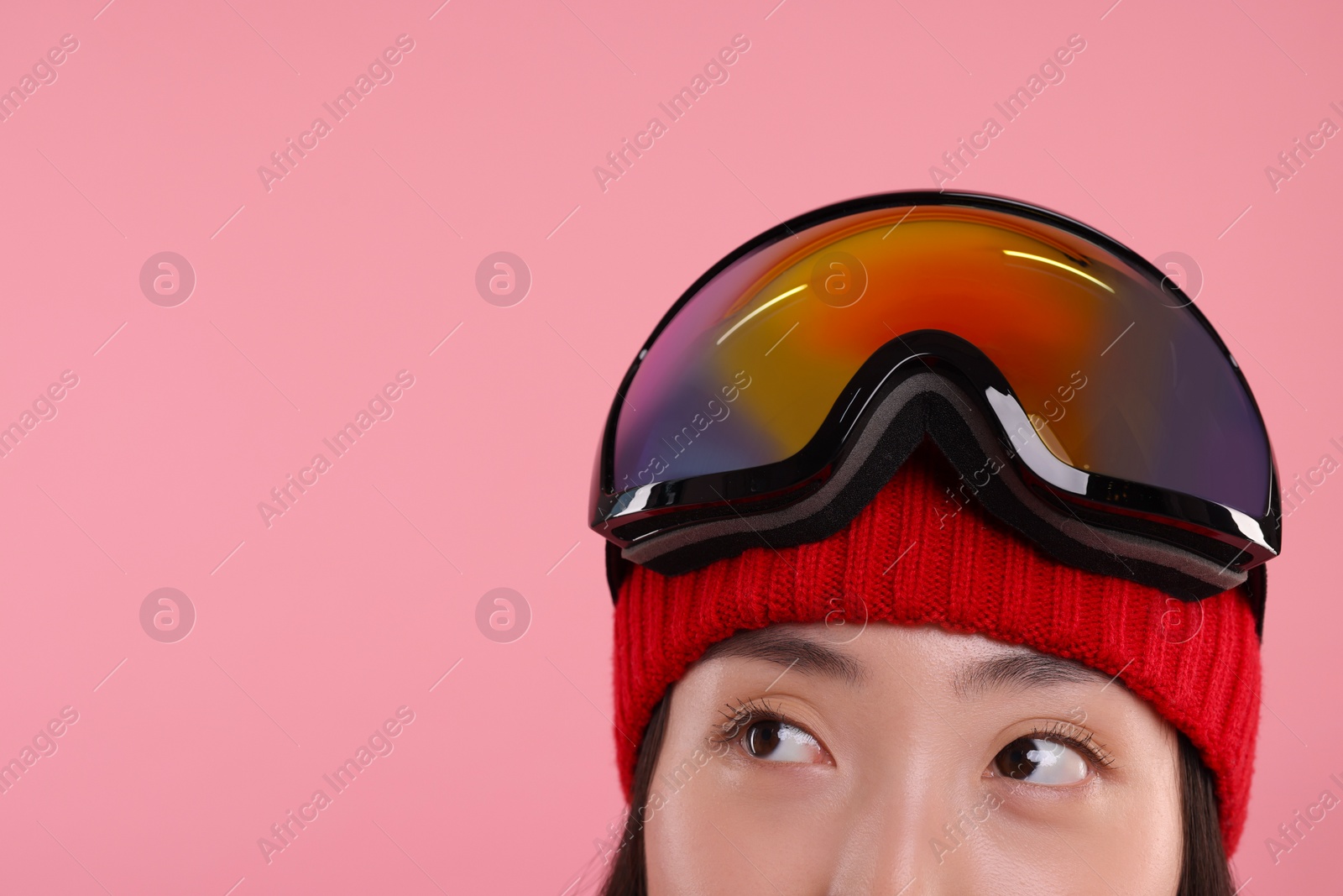 Photo of Winter sports. Woman in hat and goggles on pink background, closeup. Space for text