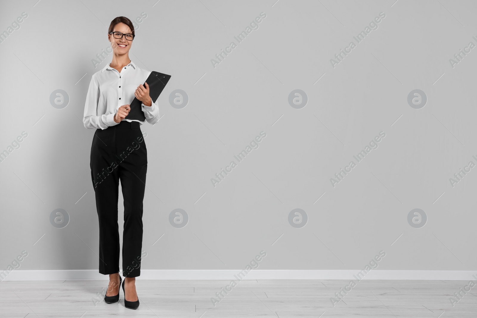 Photo of Happy secretary with clipboard and pen near light grey wall, space for text