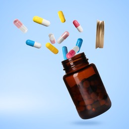 Image of Many different colorful pills falling into bottle on light blue background