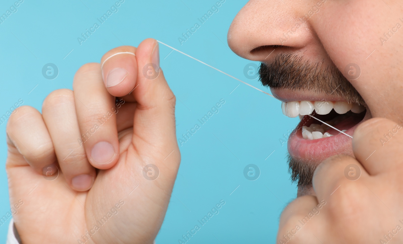 Photo of Young man flossing teeth on color background, closeup