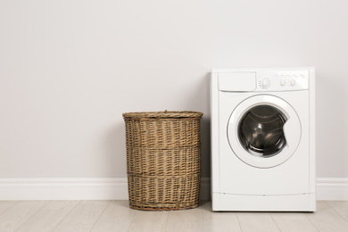 Photo of Modern washing machine with laundry basket near white wall
