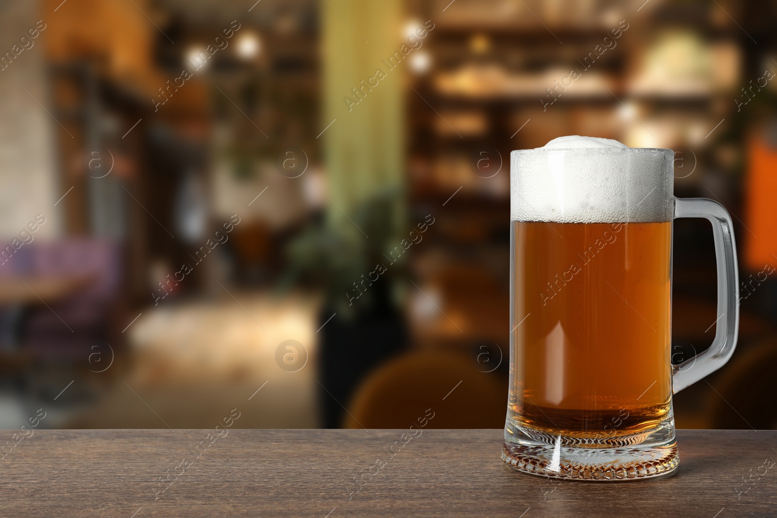 Image of Mug with fresh beer on wooden table in pub, space for text