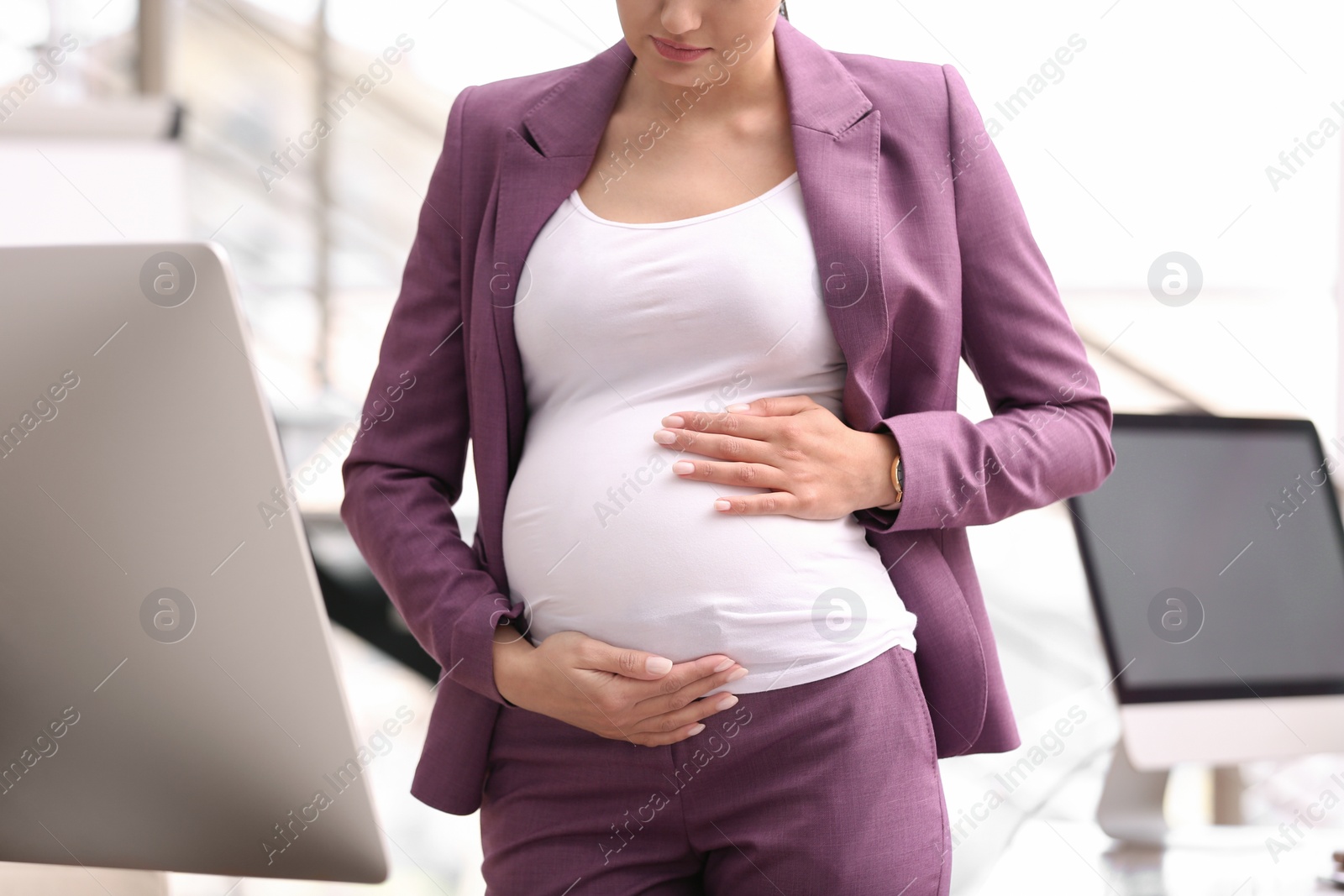 Photo of Young pregnant woman in suit at workplace, closeup