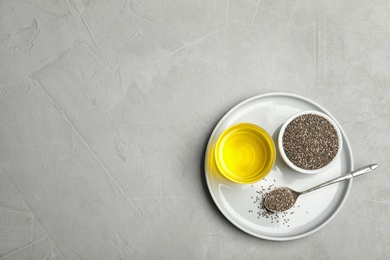 Plate with chia oil, seeds and spoon on grey background, top view. Space for text