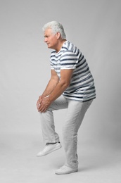 Full length portrait of senior man having knee problems on grey background