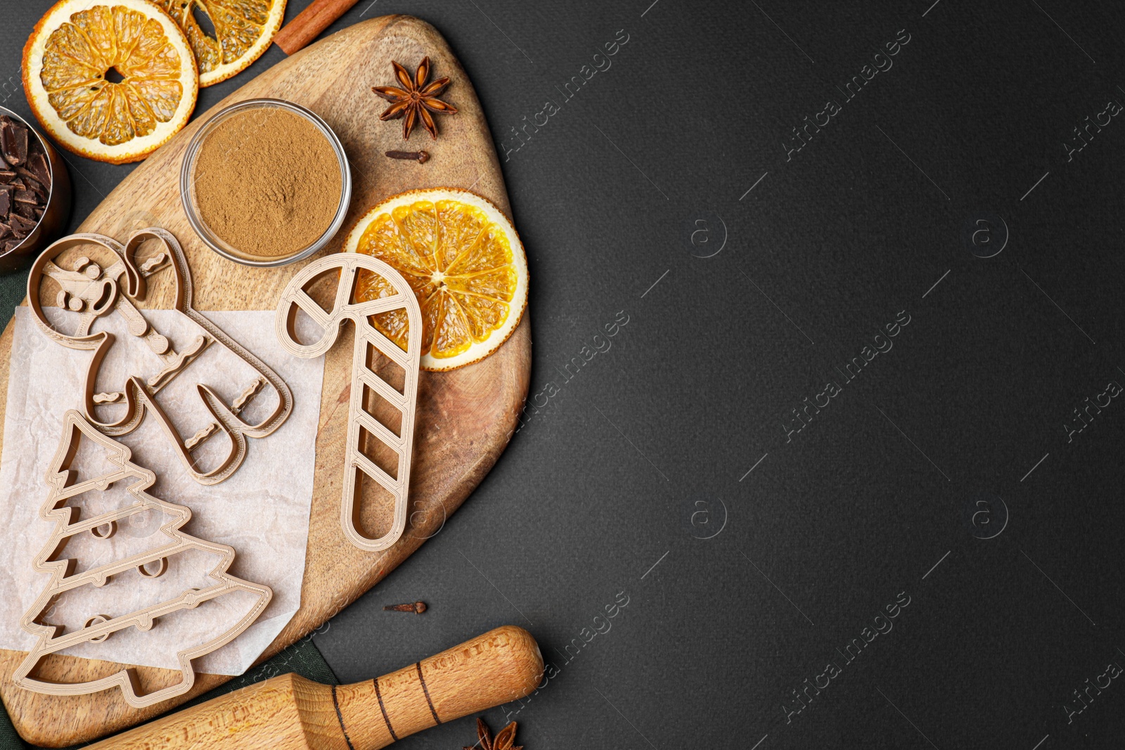 Photo of Christmas treat. Flat lay composition with cookie cutters and ingredients on black table. Space for text