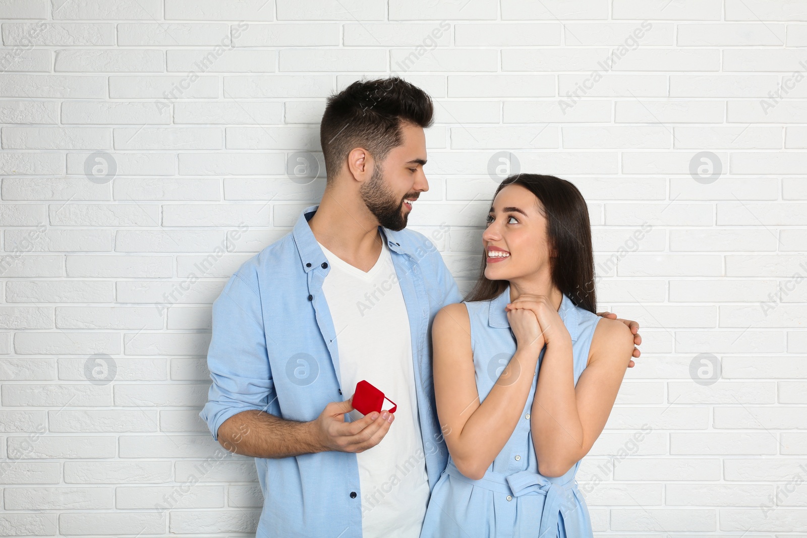 Photo of Man with engagement ring making marriage proposal to girlfriend near white brick wall