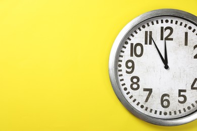 Photo of Clock showing five minutes until midnight on yellow background, space for text. New Year countdown