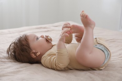Cute little baby with pacifier on bed indoors