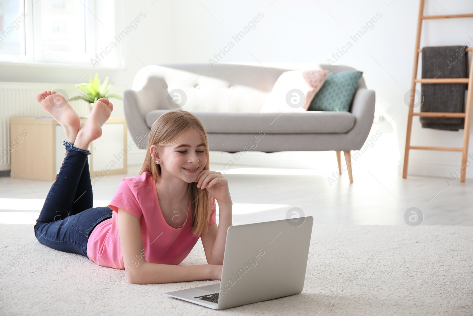 Photo of Teenage girl with laptop lying on cozy carpet at home