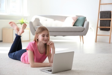 Teenage girl with laptop lying on cozy carpet at home