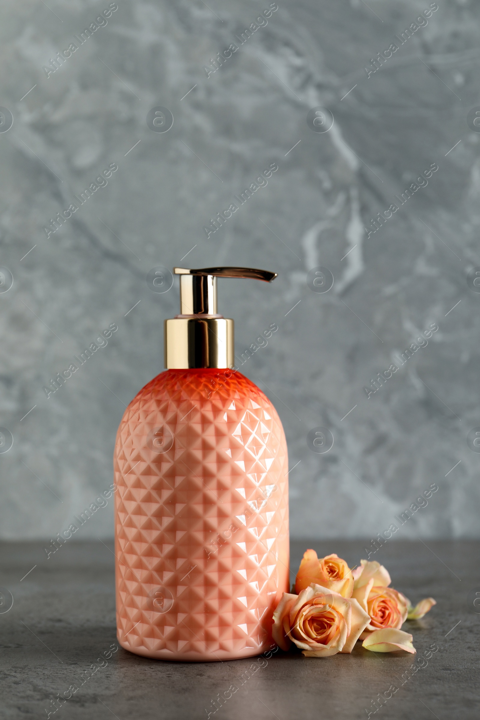 Photo of Stylish dispenser with liquid soap and beautiful flowers on grey table