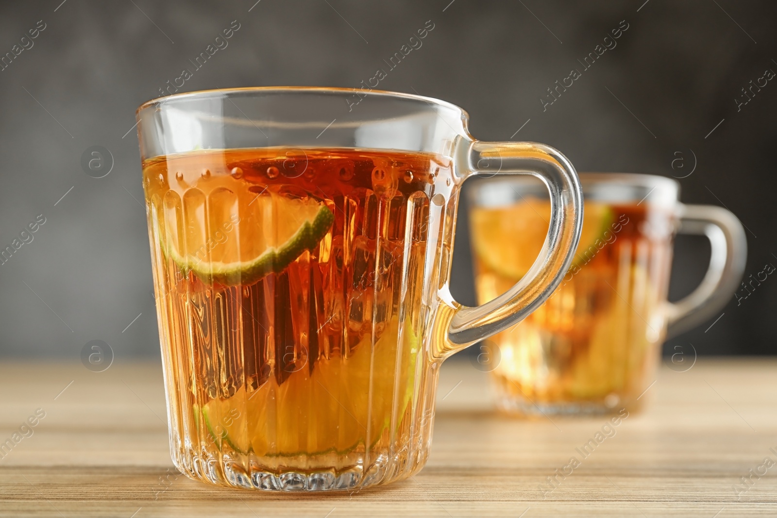 Photo of Cups of tasty ice tea with lime on wooden table against grey background