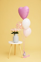 Photo of Bunch of different shaped balloons and beautiful rose flowers on coffee table for birthday party against beige background