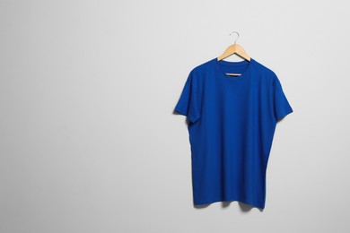 Photo of Hanger with blue t-shirt on light wall. Mockup for design