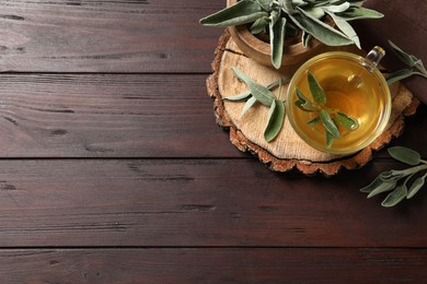 Cup of aromatic sage tea and fresh leaves on wooden table, flat lay. Space for text