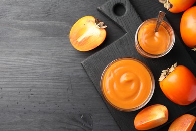 Photo of Delicious persimmon jam on dark gray wooden table, flat lay. Space for text