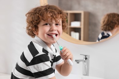 Photo of Cute little boy holding electric toothbrush in bathroom, space for text
