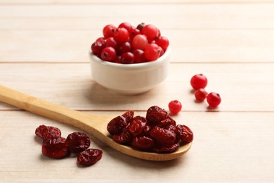 Photo of Spoon with dried cranberries and fresh berries in bowl on wooden table