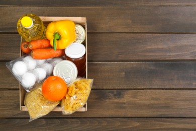 Photo of Crate with donation food on wooden table, top view. Space for text