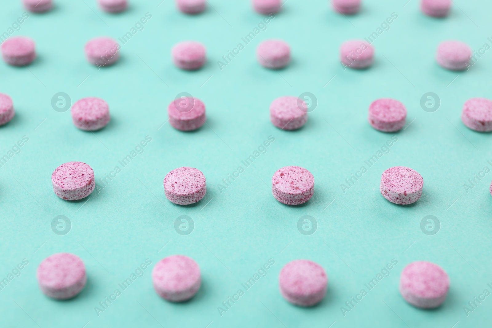 Photo of Many pink vitamin pills on turquoise background, closeup