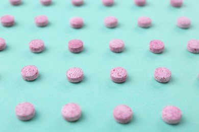Many pink vitamin pills on turquoise background, closeup