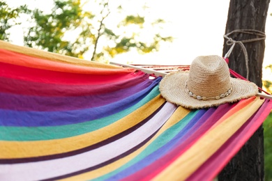 Comfortable bright hammock with wicker hat at green garden, closeup