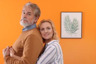 Photo of Happy mature couple hugging near orange wall. Dating agency