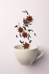 Photo of Anise stars and dry tea falling into cup on white background, flat lay