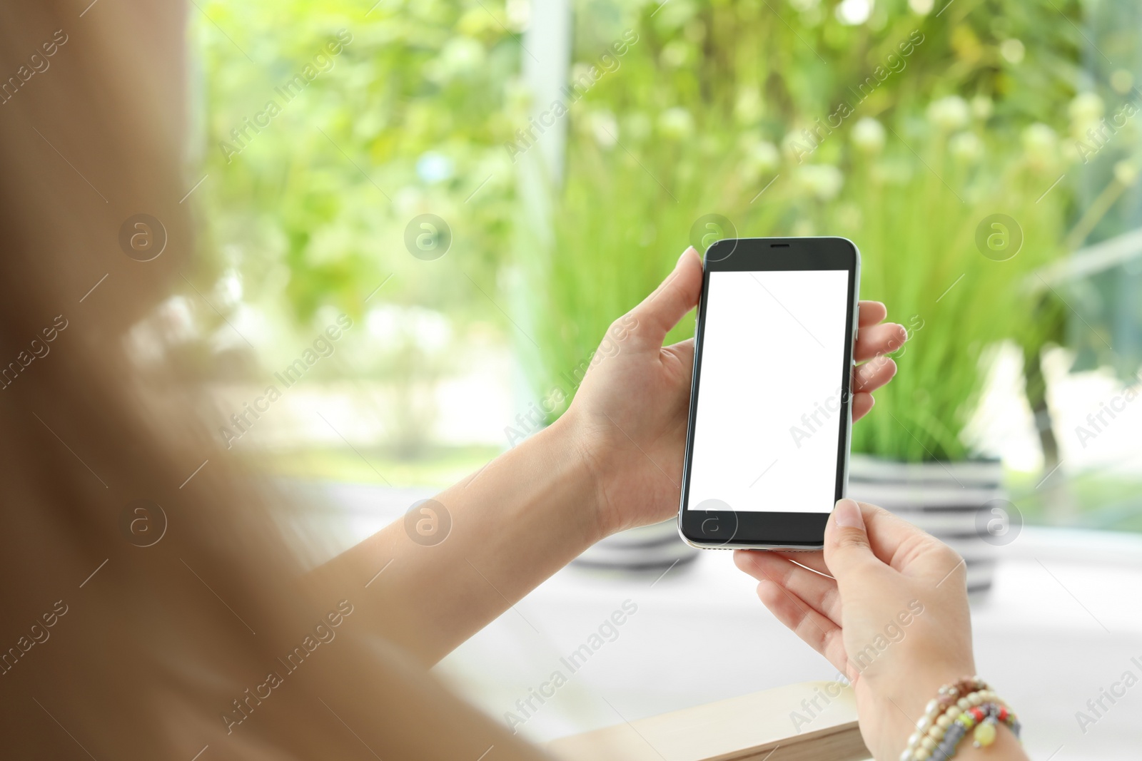 Photo of Woman holding smartphone with blank screen on blurred background. Mockup for design