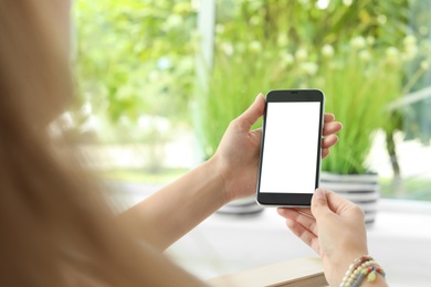 Woman holding smartphone with blank screen on blurred background. Mockup for design