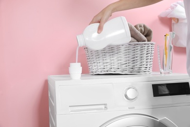 Photo of Woman pouring liquid detergent into cap on washing machine in laundry room, closeup