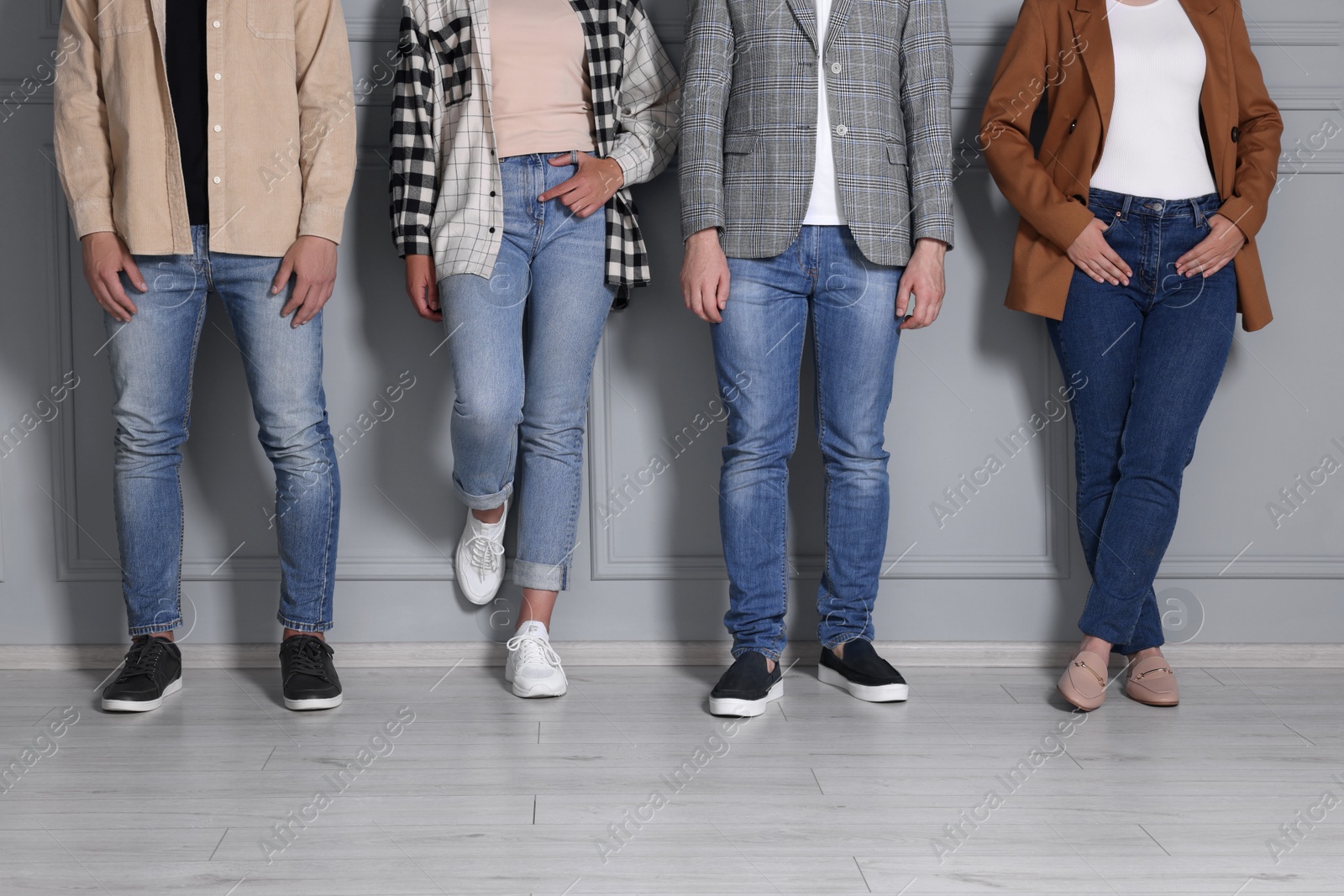 Photo of Group of people in stylish jeans near light grey wall indoors, closeup