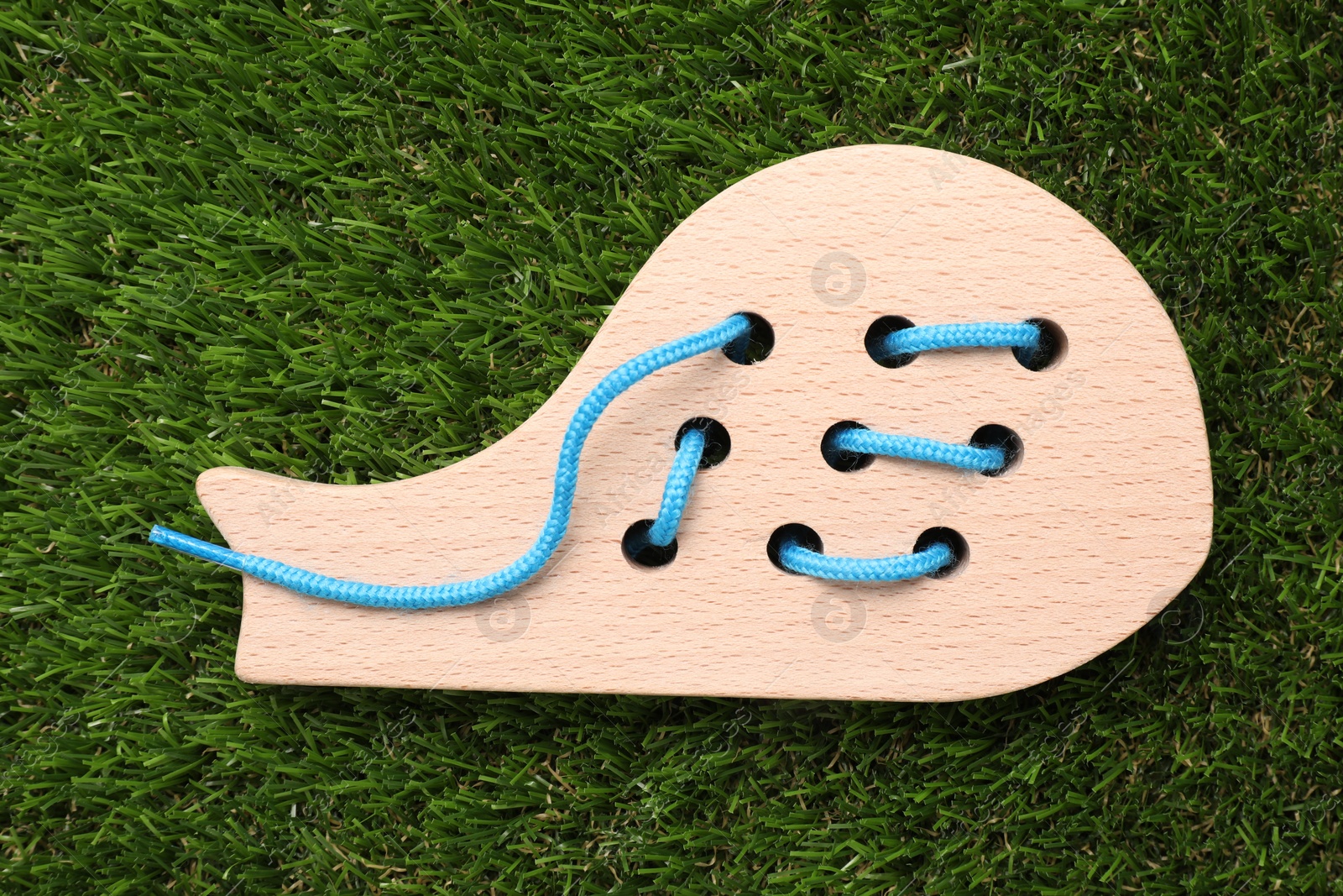 Photo of Wooden whale figure with holes and lace on artificial grass, top view. Educational toy for motor skills development