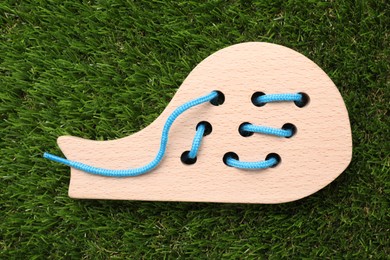 Photo of Wooden whale figure with holes and lace on artificial grass, top view. Educational toy for motor skills development