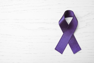 Purple ribbon on white wooden background, top view with space for text. Domestic violence awareness
