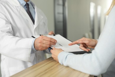 Photo of Doctor with clipboard consulting patient in clinic, closeup
