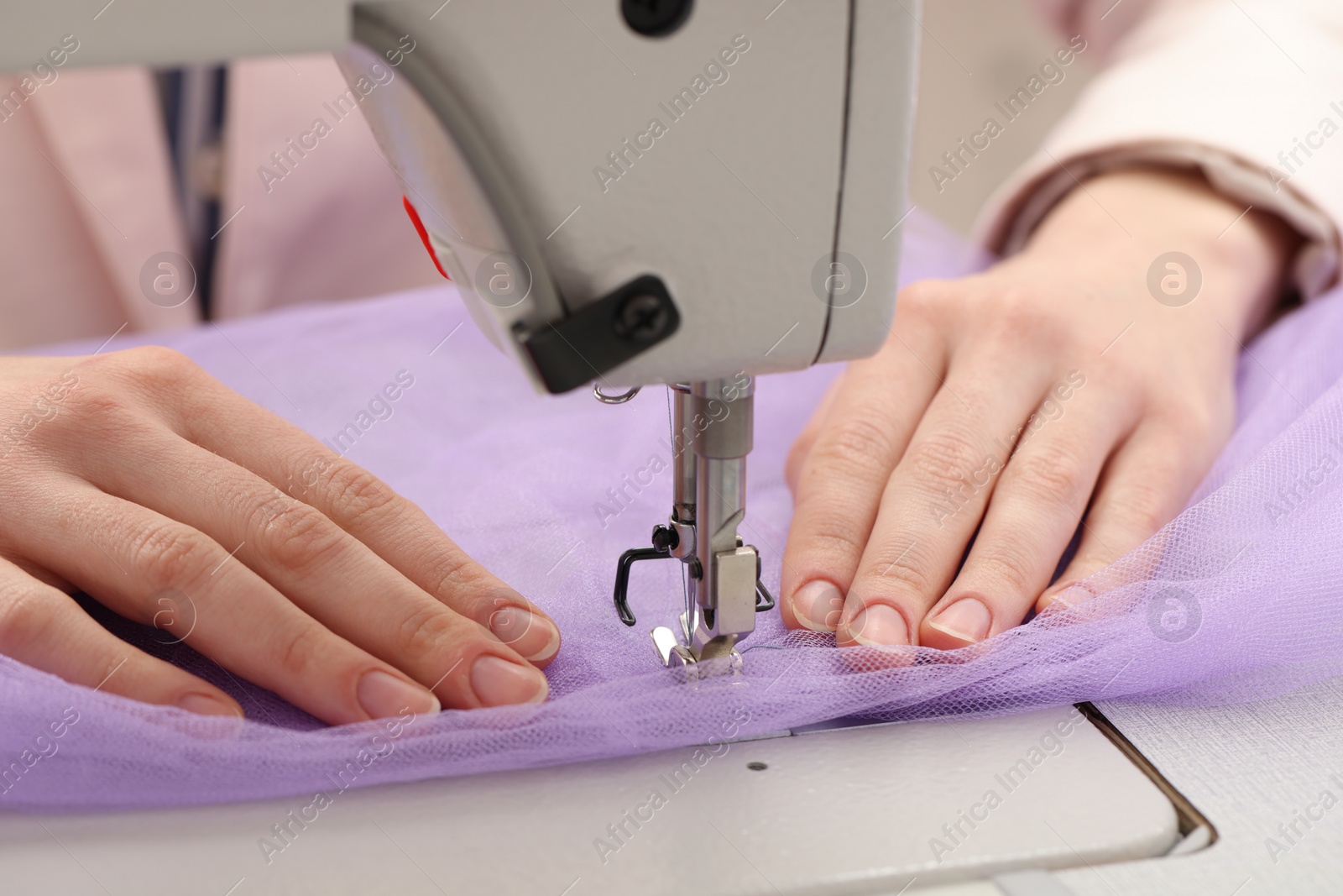 Photo of Dressmaker sewing new dress with machine in atelier, closeup