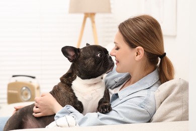 Photo of Happy woman hugging cute French Bulldog on sofa in room