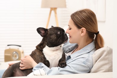 Happy woman hugging cute French Bulldog on sofa in room